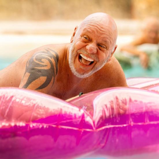 Mand griner i vandet ved en oppustelig, lyserød badebold.